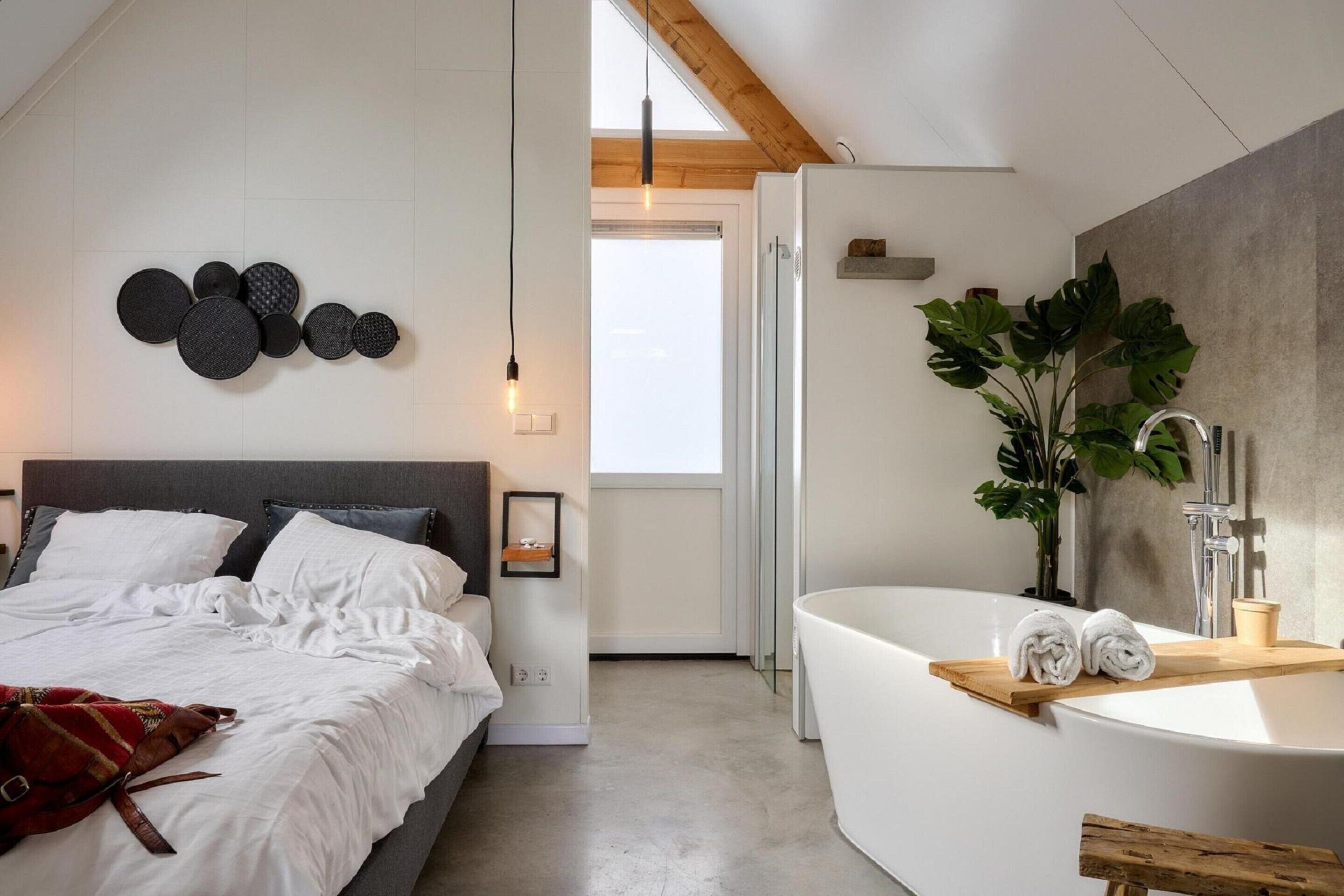 A modern bedroom with a large bed, a wall-mounted light fixture, and a view of the bathroom.