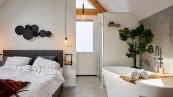 A modern bedroom with a large bed, a wall-mounted light fixture, and a view of the bathroom.