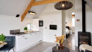 Une cuisine moderne avec des armoires blanches, une cuisinière à gaz et un évier. On y trouve un coin repas avec une table ronde et des chaises. Une cheminée est visible au fond.