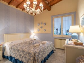 Une chambre à coucher comprenant un lit, des tables de chevet, un lustre, une fenêtre avec des rideaux et des éléments de décoration murale.