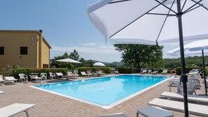 A swimming pool with lounge chairs and umbrellas, surrounded by a brick patio and a building with a yellow facade. - Belvilla by OYO Selvatello Villino Trilo (Casole d'Elsa)