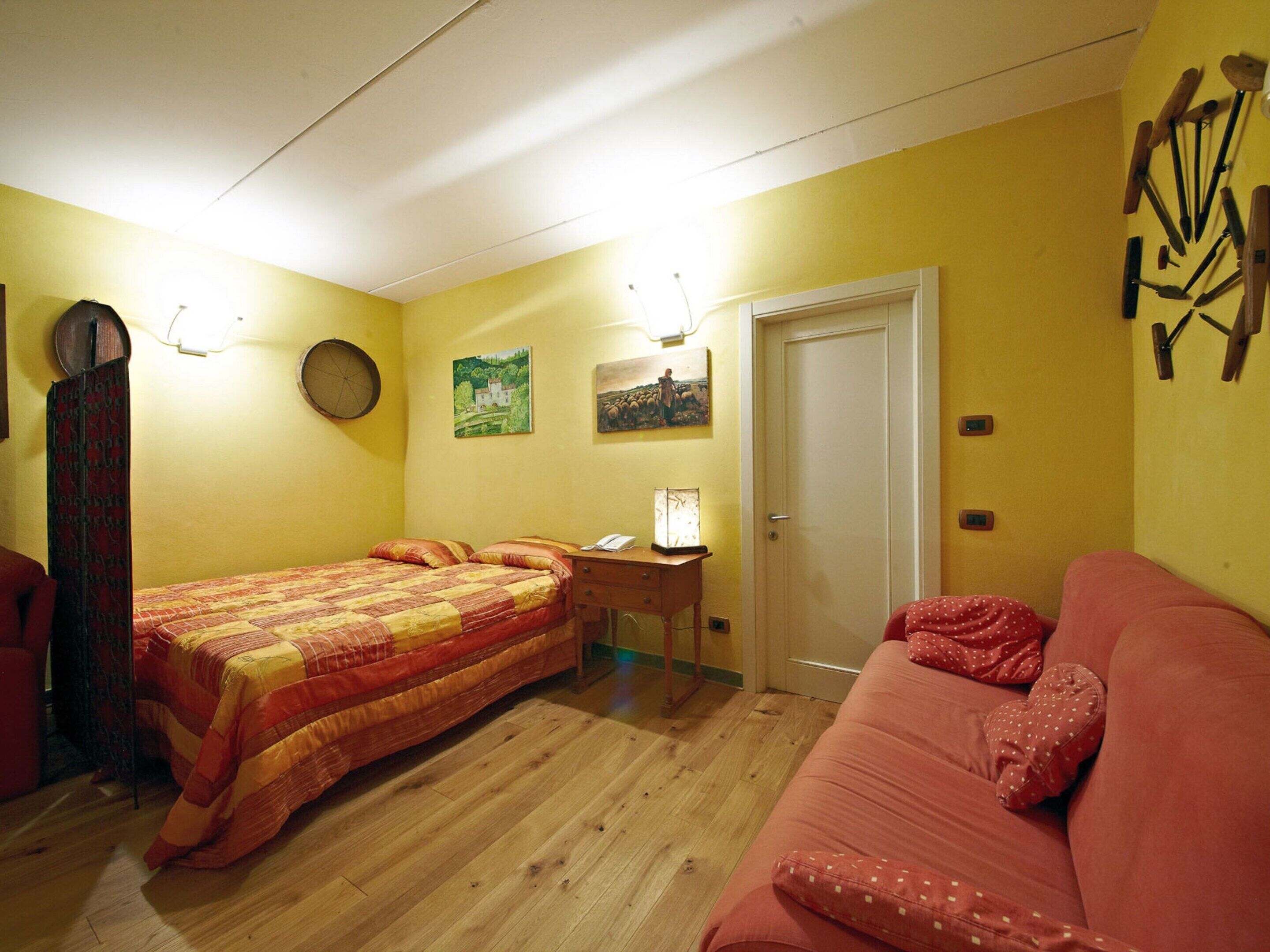 A bedroom with a bed, a desk, a chair, a sofa, and a door.