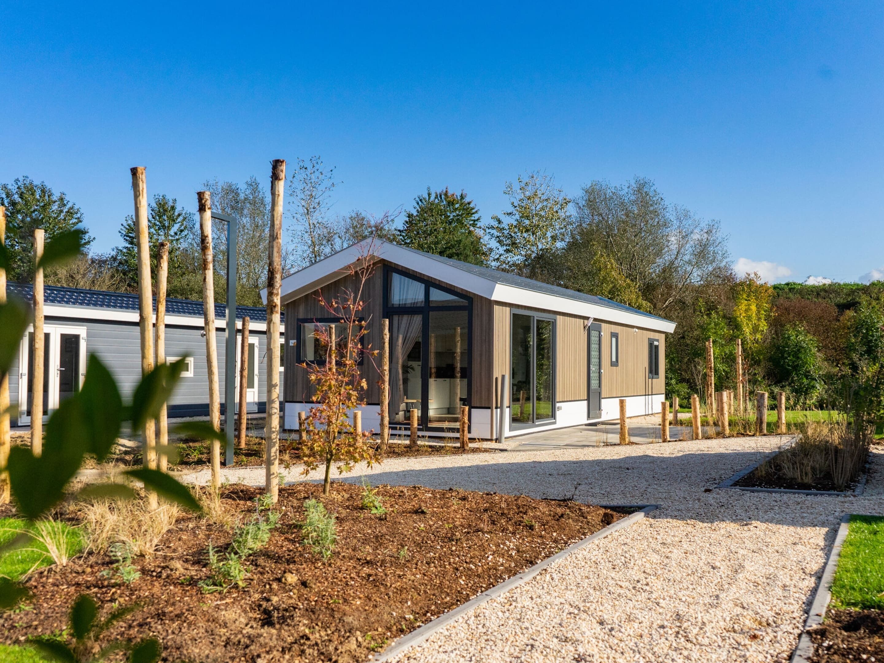 A modern single-story house with a large glass door and windows, surrounded by a gravel driveway and a garden area.
