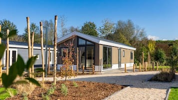 A modern single-story house with a large glass door and windows, surrounded by a gravel driveway and a garden area.