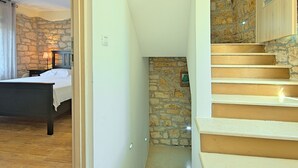 A bedroom with a bed, a nightstand, and a stone wall. - Perfect for Children, Garden With Pool, Playground and Walk in Whirlpool (Tinjan)