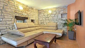 A living room with a stone wall, a sectional sofa, a wooden coffee table, and a potted plant. - Perfect for Children, Garden With Pool, Playground and Walk in Whirlpool (Tinjan)