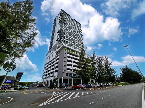 A modern high-rise building with multiple floors, a parking area in front, and a clear blue sky with clouds. - Swan Garden Resort Hotel (Malacca City)