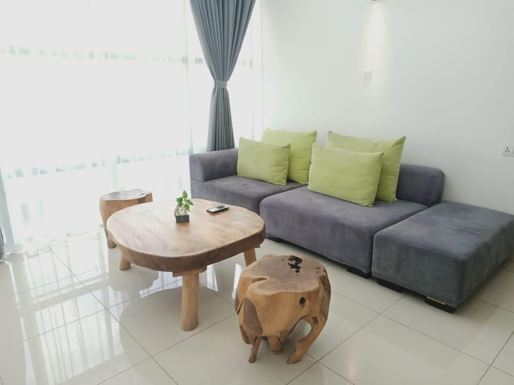 Una sala moderna con un sofá gris, cojines verdes, una mesa de centro de madera y un taburete pequeño de madera.
