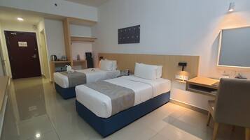 A hotel room with two beds, a desk, a chair, a flat-screen TV, and a wall-mounted shelf with items.