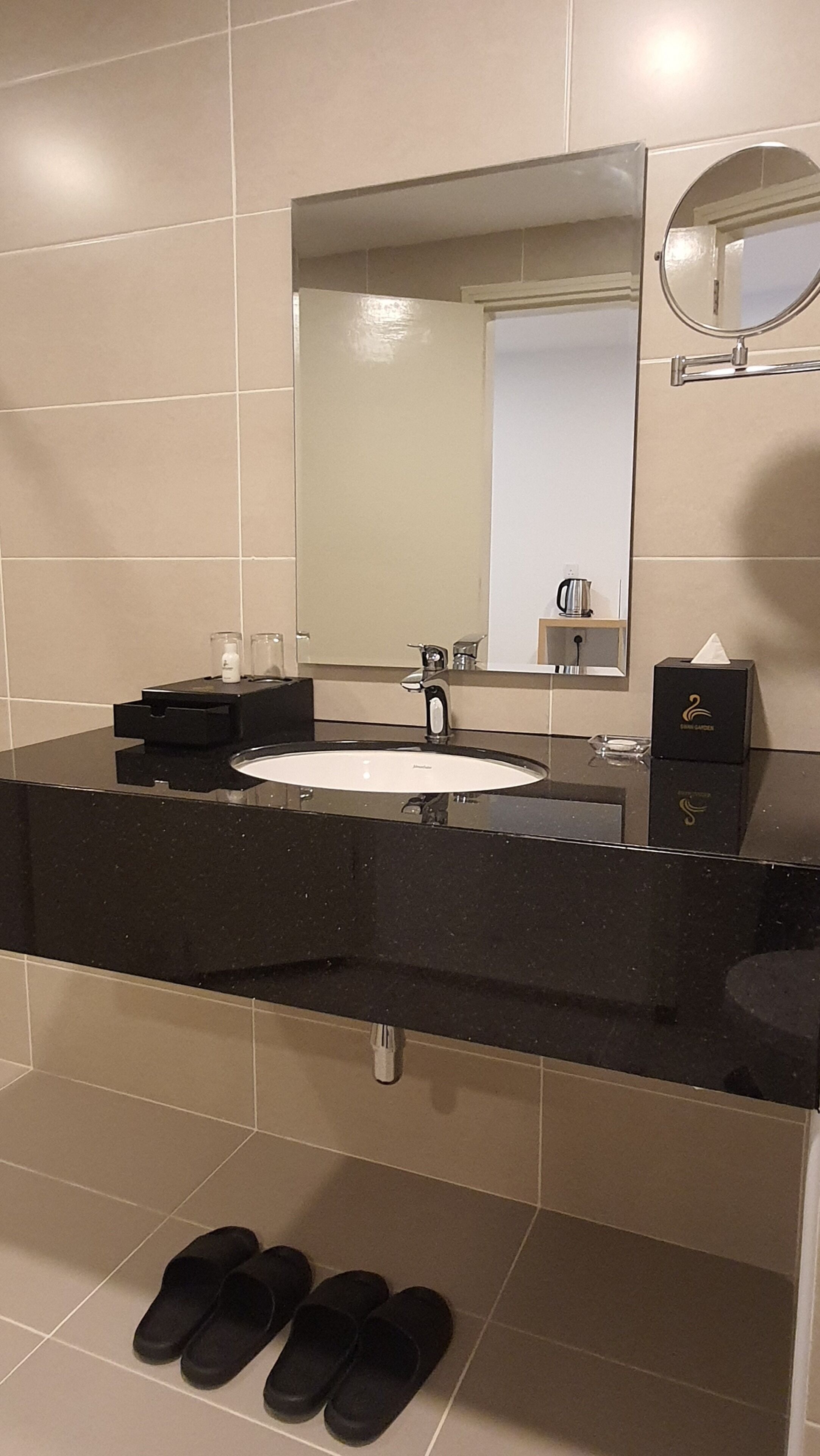 A bathroom with a black countertop, a white sink, a mirror, and a pair of slippers on the floor.