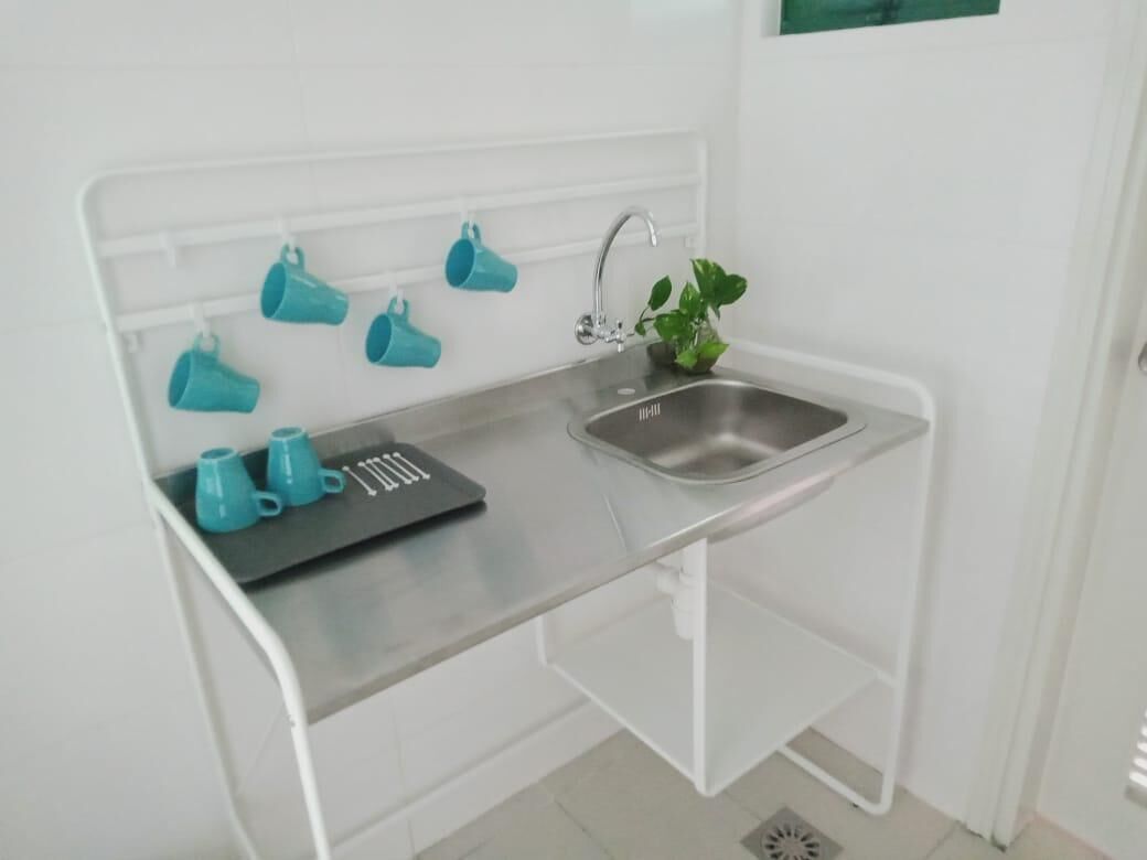 A compact kitchen with a stainless steel sink, a white countertop, and a drying rack with teal mugs.