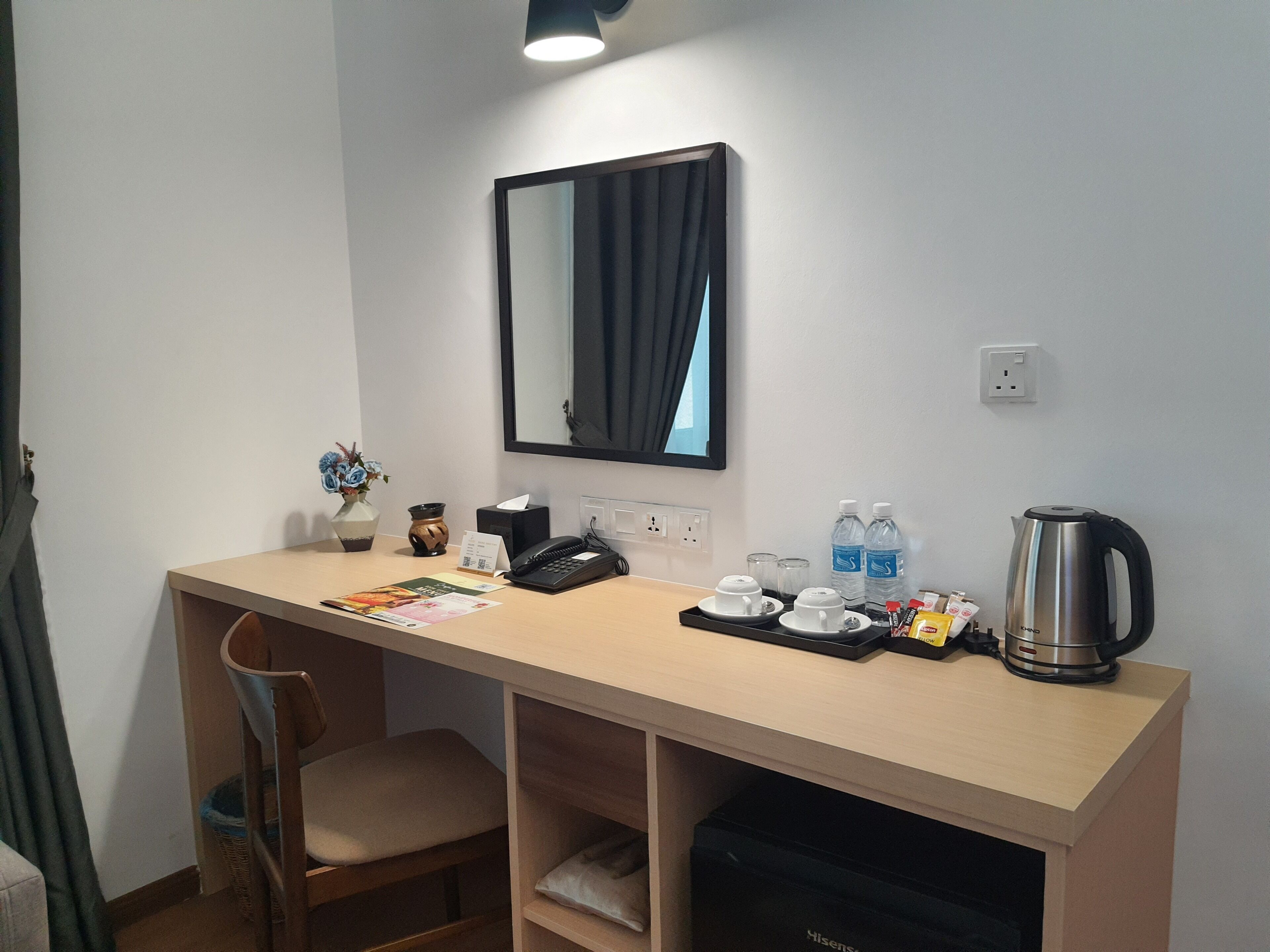 A hotel room with a desk, chair, mirror, and a kettle.