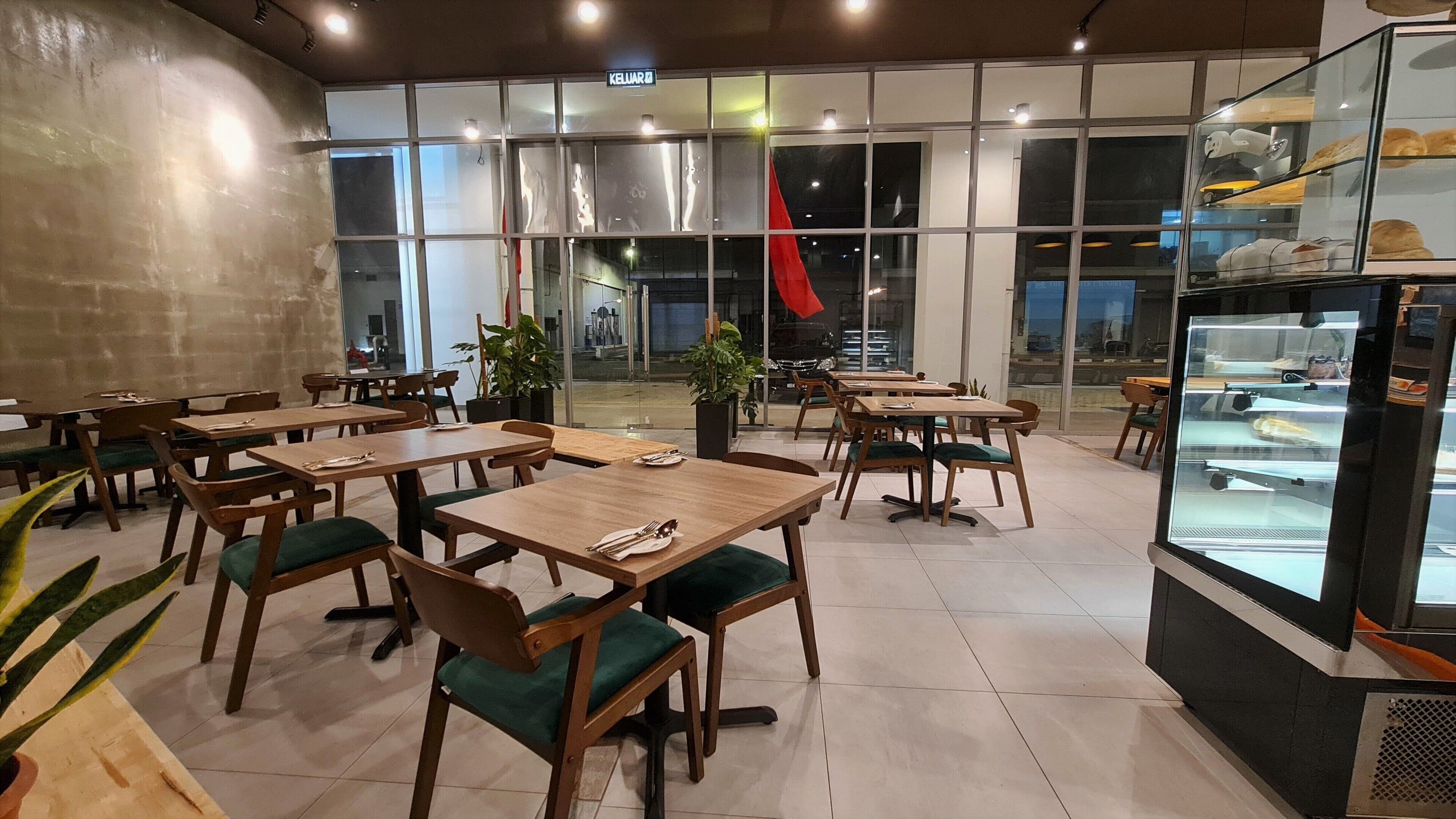 A restaurant with wooden tables and chairs, large windows, and a display case with food items.