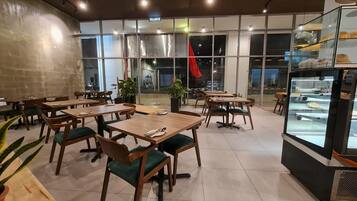 A restaurant with wooden tables and chairs, large windows, and a display case with food items.