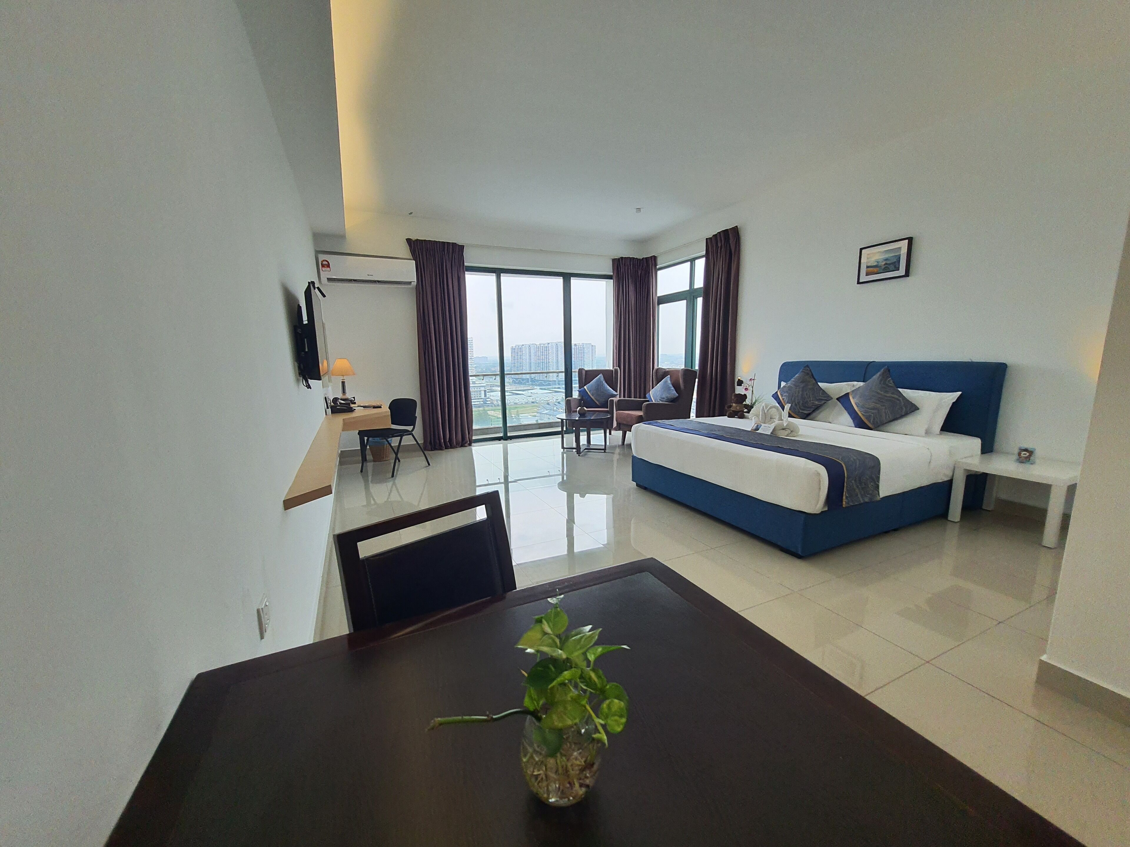 Habitación de hotel con una cama grande, un escritorio con una silla, un televisor y vistas a la ciudad.
