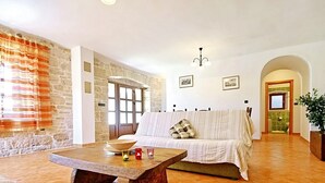 Un salon avec un mur en pierre, une table basse en bois, un canapé à rayures et une porte donnant sur une autre pièce.