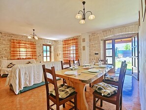 A dining area with a stone wall, a wooden table set for four, and a view of the outside. - Authentic Villa in Tinjan With Private Pool (Tinjan)