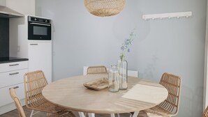 A modern kitchen with white cabinetry, a built-in oven, and a round dining table with wicker chairs. - Luxury Lodge with 2 Bathrooms near Markermeer (Wijdenes)
