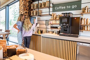 A coffee shop interior with a coffee machine, shelves with coffee bags, and a sign that reads 'Coffee to go'.