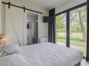 A bedroom with a bed, a television mounted on the wall, and a sliding door leading to a bathroom. - Luxury Lodge with 2 Bathrooms near Markermeer (Wijdenes)