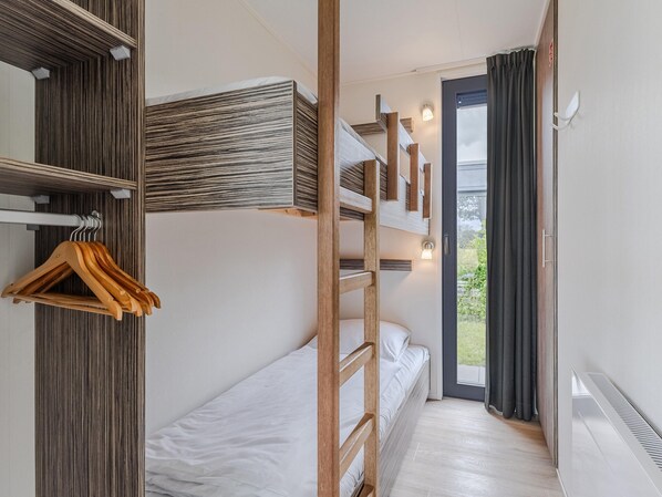Habitación con literas, una escalera de madera, un perchero y una puerta corrediza que da a un balcón.