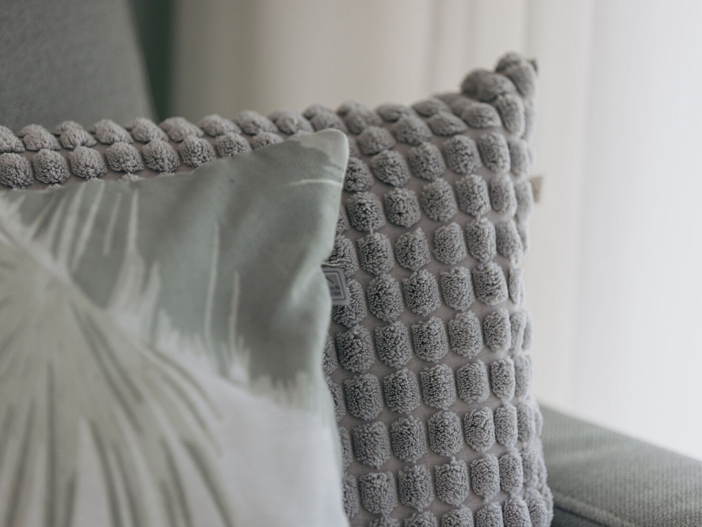 Nærbillede af en struktureret grå pude og en glat grå hynde på en sofa.