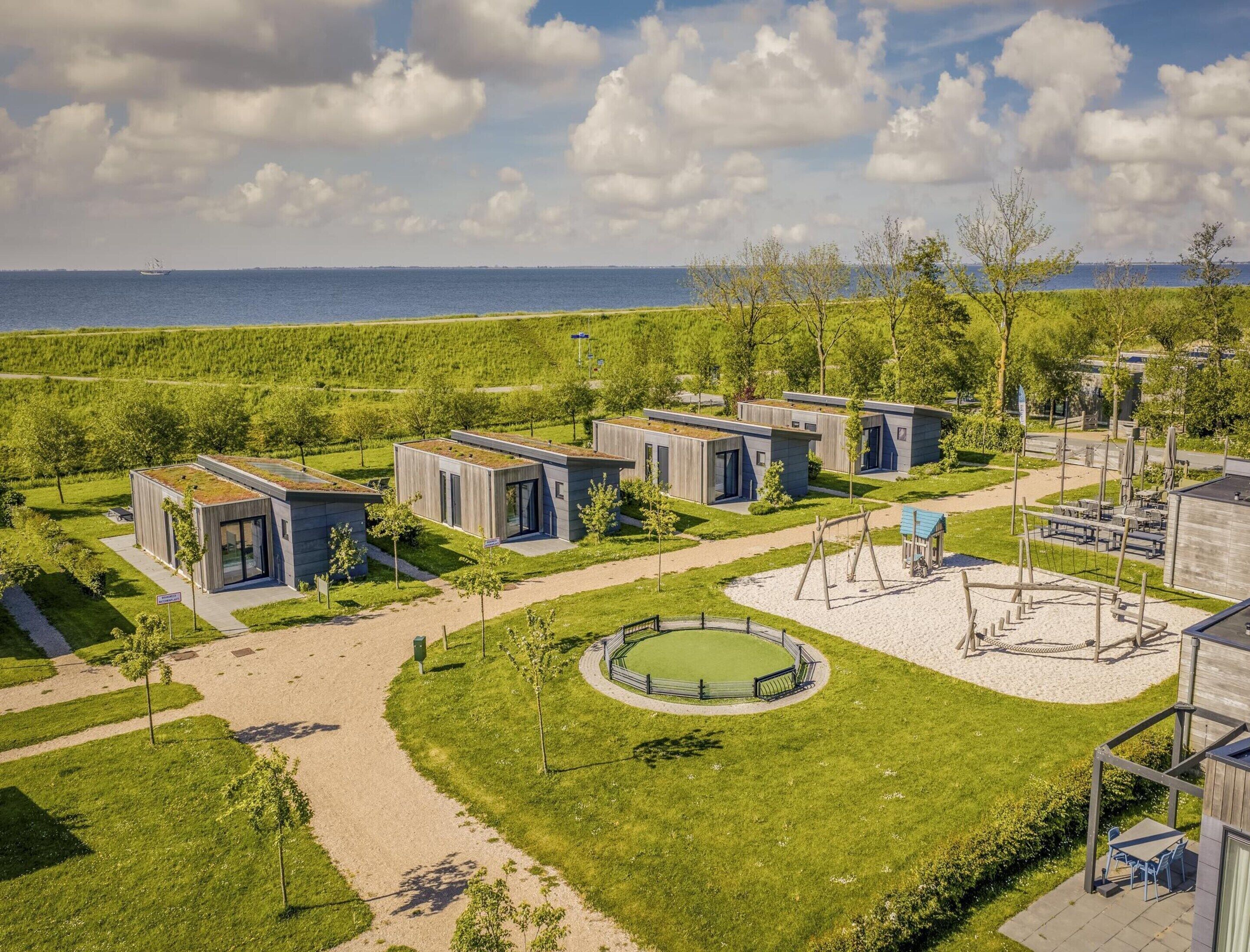 Un quartier résidentiel moderne avec des maisons compactes, une aire de jeux circulaire et une vue sur la mer.