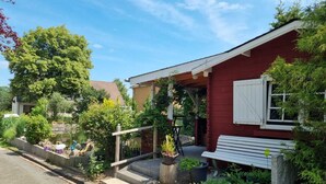 Een rood huis met een witte luik, een bankje en een kleine tuin met een trap naar de ingang.