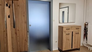 Een kamer met een houten garderobe, een blauwe deur en een spiegel aan de muur.