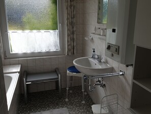 A bathroom with a white sink, a mirror, a window with a frosted glass, and a tiled floor.