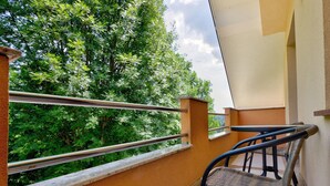 A balcony with a metal railing, a wicker chair, and a view of lush green trees. - Charming Apartment in Bled Near Lake (Bled)