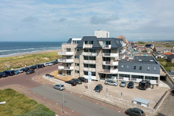 Et hotel med flere etager, altaner, parkeringsplads og udsigt til strand og hav.