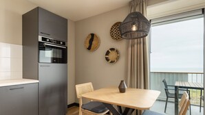 A modern kitchen with a built-in oven and a dining area with a wooden table and two chairs. - Apartment in Egmond by the Beach (Egmond aan Zee)