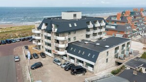 A multi-story hotel with a stone facade, balconies, and a parking area in front. - Apartment in Egmond by the Beach (Egmond aan Zee)