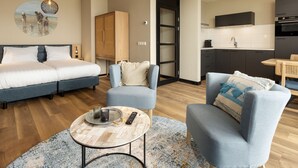 A modern hotel room with a bed, two armchairs, a small round table with a tray, a remote control, and a wall-mounted TV. - Apartment in Egmond by the Beach (Egmond aan Zee)