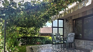Eine überdachte Terrasse mit einer Pergola, Steinmauern und Blick auf ein Gebäude mit einem Fenster.