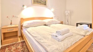 Ein ordentlich bezogenes Bett mit Kopfteil, ein Nachttisch mit Lampe und ein an der Wand hängendes Bild.