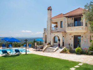 Uma casa de pedra de dois andares com piscina, área de estar ao ar livre e vista para as montanhas.