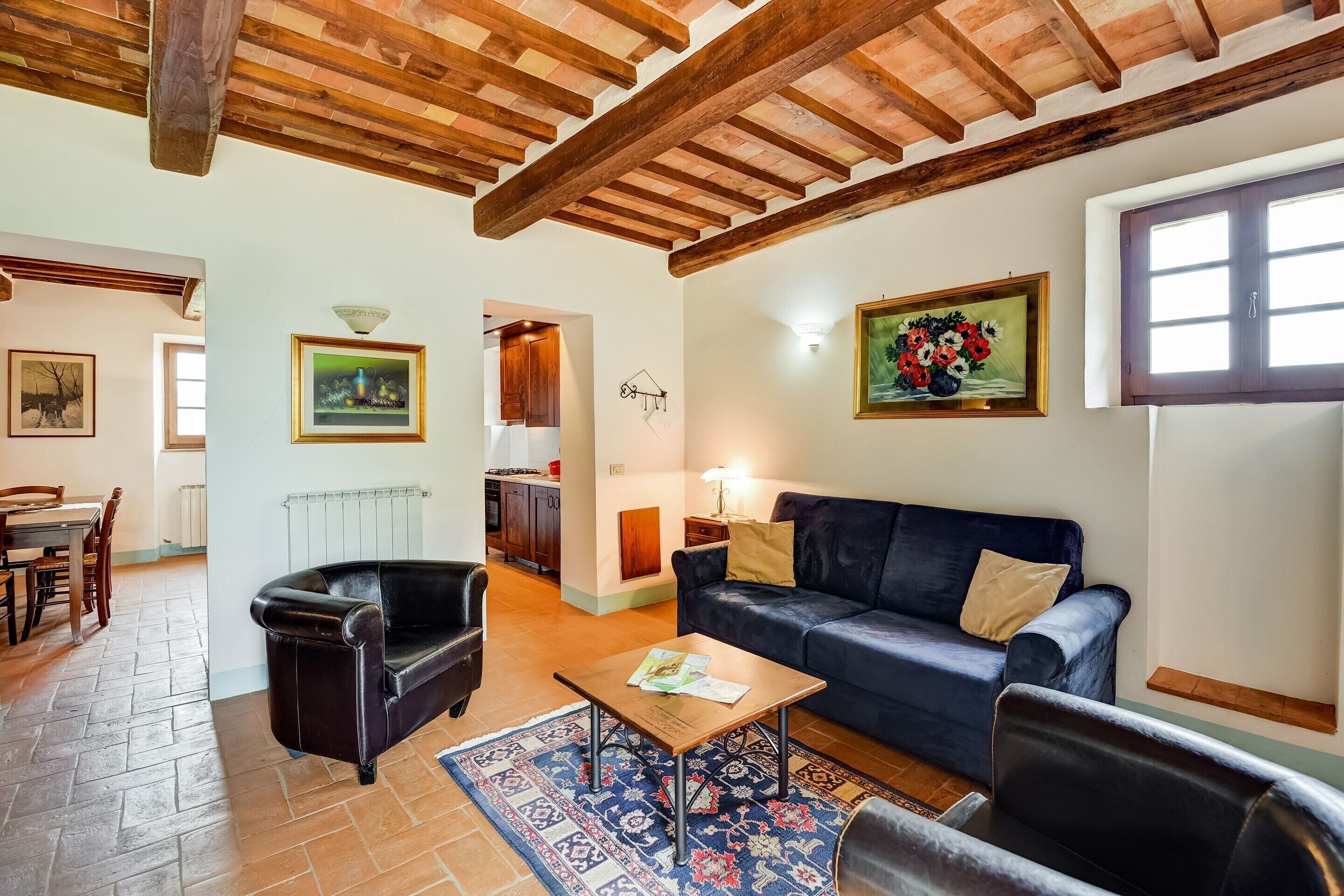 Un salon avec un canapé bleu foncé, un fauteuil en cuir noir et une table basse en bois. Un tapis à motifs recouvre le sol, et le salon est doté de poutres apparentes en bois au plafond.
