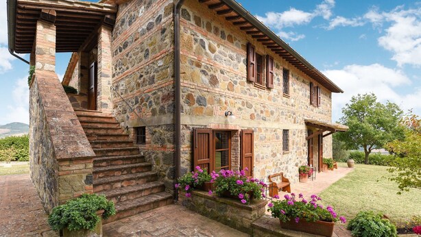 A stone house with a wooden staircase, a covered porch, and a garden with potted plants. - Belvilla by OYO Piandigoro Intero (Radicofani)