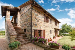 A stone house with a wooden staircase, a covered porch, and a garden with potted plants. - Belvilla by OYO Piandigoro Intero (Radicofani)
