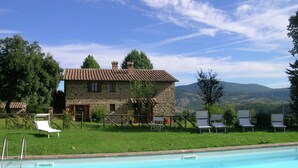 A stone building with a tiled roof, a swimming pool, and lounge chairs. - Belvilla by OYO Piandigoro - I Lecci (Radicofani)