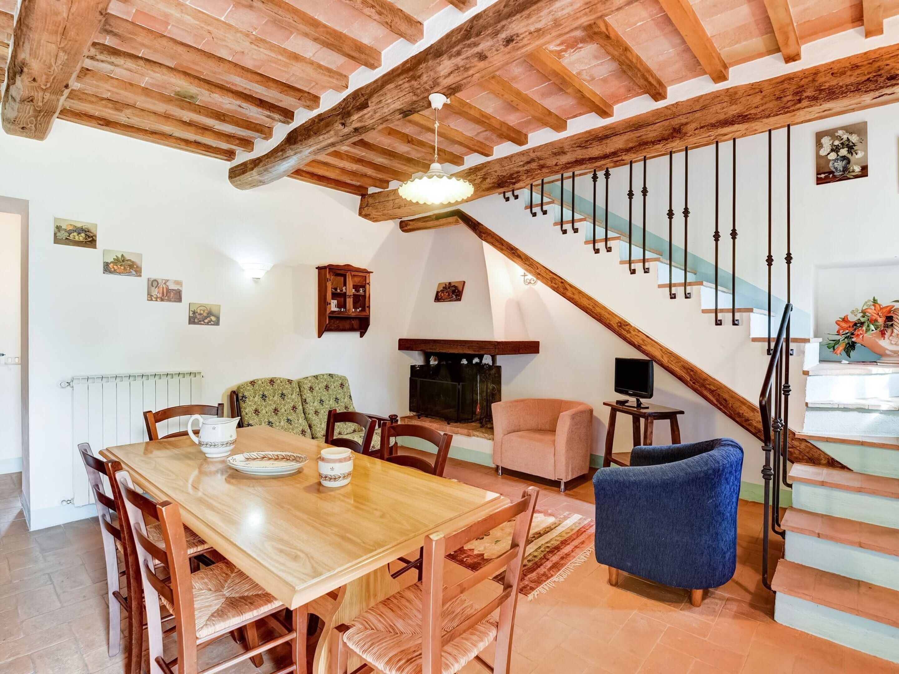 Een eethoek met een houten tafel en stoelen, een bank, een televisie en een trap met een houten leuning.