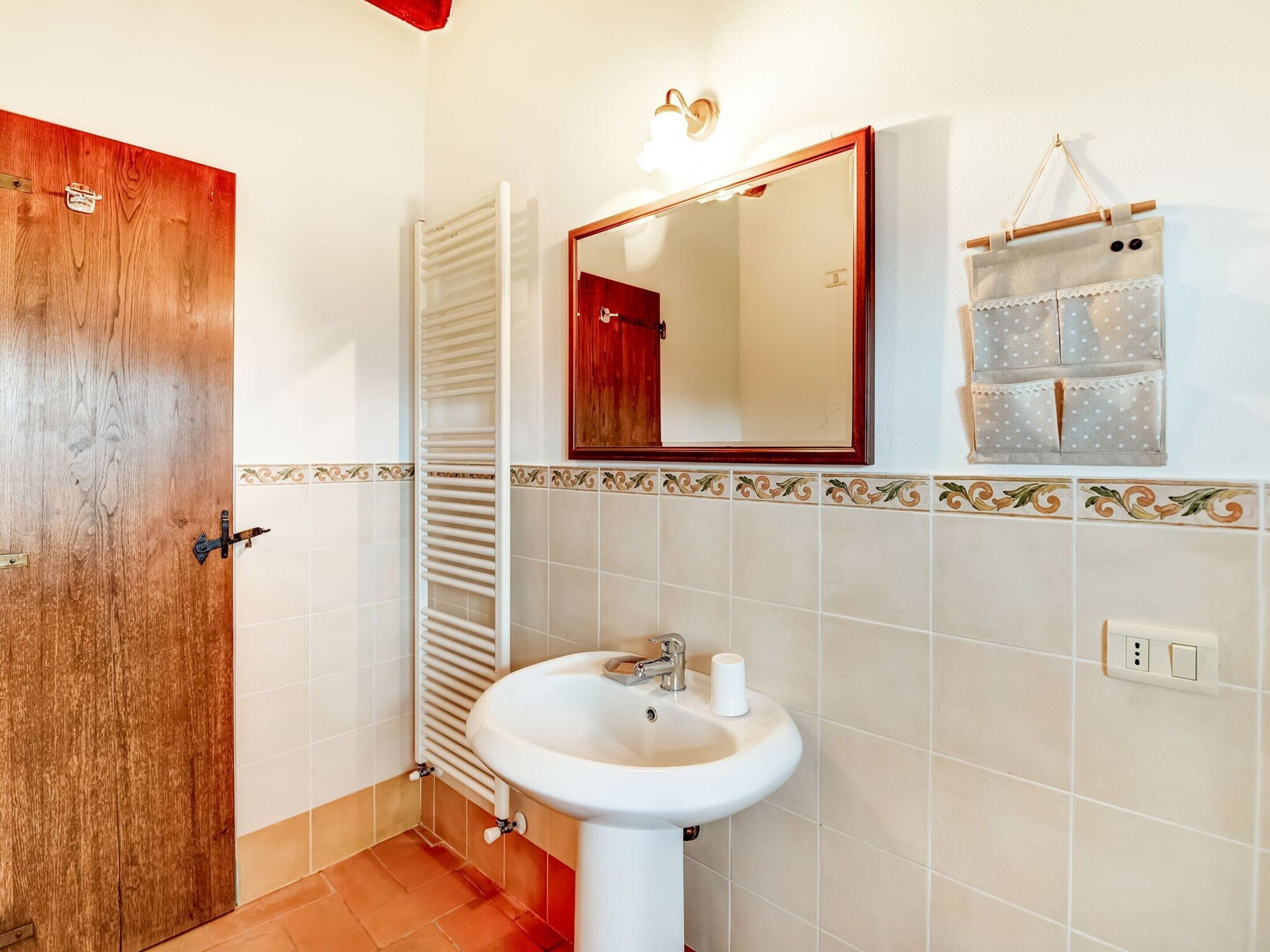 A bathroom with a wooden door, a white sink, a towel rack, a mirror, and a small toiletry bag.