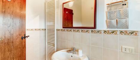 A bathroom with a wooden door, a white sink, a towel rack, a mirror, and a small toiletry bag.