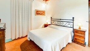 A bedroom with a bed, wooden headboard, nightstands, a lamp, a painting, and a window with curtains. - Belvilla by OYO Piandigoro - I Lecci (Radicofani)