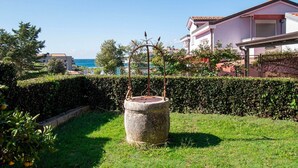 Un jardin avec une fontaine en pierre, une haie et un bâtiment avec un toit rouge en arrière-plan.