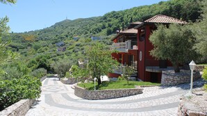 Un bâtiment rouge avec un chemin de pierre menant à l’entrée, entouré de verdure et de collines.