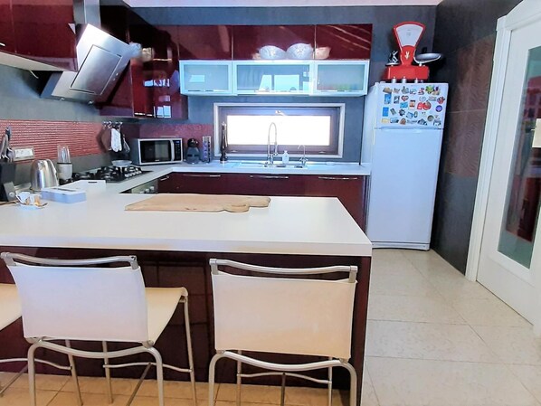 Una cocina moderna con una isla central, sillas blancas, microondas, estufa y refrigerador con imanes.