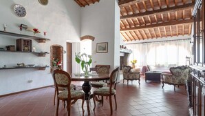 A spacious living room with a high wooden ceiling, a dining area with a round table and chairs, and a fireplace. - Tuscan Farmhouse in Peccioli with Swimming Pool near Lakes (Peccioli)